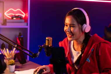 İnternet üzerinden kulaklık takıp gülümseyen Asyalı güzel kız flamasının sunucu kanalı izleyicilerle internet üzerinden konuşma yapıyor. Esport yetenekli takım oyuncuları neon mavi odada. Taktik.