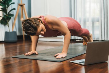 Spor kıyafetleri içinde esnek ve becerikli bir kadın evde egzersiz paspası üzerinde meditasyon pozisyonunda yoga yapıyor. Huzurlu bir zihin ve sükunetle evde yoga eğitimi..