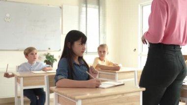 Asyalı mutlu öğrenci ilköğretim sınıfında soruları cevaplamak için gönüllü olurken öğretmen tahtaya cevap yazmak için öğrenciyi seçiyor. Sınıfta çeşitli çocuklar var. Pedagoji.
