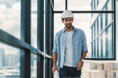 Akıllı inşaat mühendisi ev modeli ve mimari ekipmanlara bakarken ayakta duruyor, yürüyor. Kasklı bir mühendis bina modelinin yanında dururken şehir manzarası yakınında duruyor. İzleme.