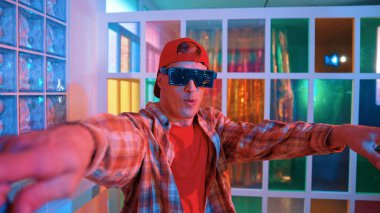 Komik break dansçı kameraya bakarken hip hop 'a doğru serbest adım atıyor. Çılgın mutlu hipster dans edip sokak dansı yaparken Led ışığında günlük kıyafet ve güneş gözlüğü takıyor. Mutluluk.