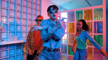 Asyalı adam gece kulübünde çeşitli neon ışıklarda dans ederken kolunu oynatıyor. Modern kulüpte çok kültürlü hippilerle dans eden şık elbiseli mutlu dansçı. Mutluluk.