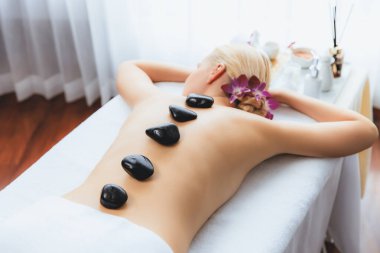 Lüks tatil köyündeki kaplıcalarda sıcak taş masajı. Gün ışığı sükunet ortamında, mutlu kadın müşteri bazalt taş masajından zevk alıyor. Rahatlatıcı bir sıcaklıkla vücudun üzerinde süzülüyor. Sessiz.