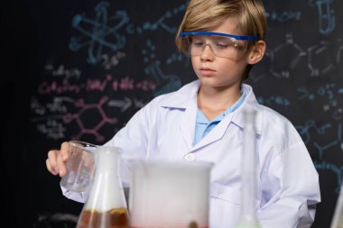 Laboratuvardaki sarışın çocuk laboratuvar önlüğü giyer ve STEM sınıfında kimya bilimi öğrenir. Öğrenci cam şişeye sıvı döker. Masaya bir sürü şişe koy. Etkinlik.
