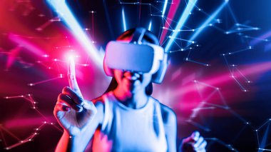 Zeki bir kadın, metaevreni birbirine bağlayan VR kulaklık takan neon ışıklarla çevrili duruyor. Gelecekteki siber uzay topluluğu teknolojisi. Sanal objeye parmağını kullanan zarif bir kadın. Halüsinasyon.