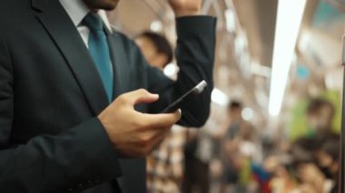 İş adamının elleri trende insanlarla çevriliyken telefona bakarken yakın çekim. Kafkas proje yöneticisi e-postaları kontrol ediyor, arka planı bulanık pazarlama stratejisi planlıyor. Sevinçli..