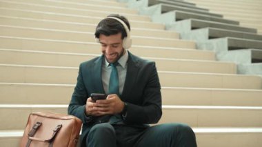 Profesyonel zeki iş adamı merdivenlerde yatarken müzik dinliyor. Akıllı yönetici iyi haberler alırken ya da kulaklıktan proje alırken mutlu olur. Yatırımcı otururken takım elbise ve çanta giyer. Sevinçli..