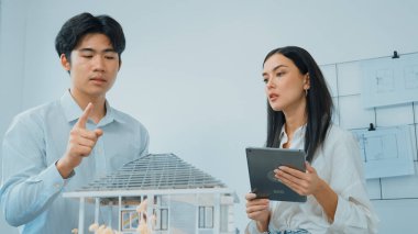 Güzel, genç, beyaz bir proje yöneticisi Asyalı mühendise, mühendislik masasında ev modelini ölçerken tablet kullanarak bina detaylarını anlattı. Tertemiz.