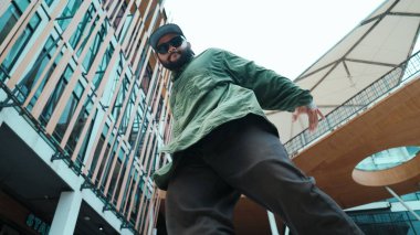 Hip hop tarzında düşük açılı hipster pozu alışveriş merkezi manzarasıyla çevrili. Kameraya bakarken dans eden Asyalı hip hop koreografının portresi. Açık hava sporu 2024. Hiphop.