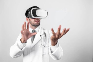 Zeki doktor, kameraya bakıyor ve beyaz arka planda duruyor. Sanal gerçeklik ya da metadünya giyerken tıbbi verileri elinde tutan ve kontrol eden beyaz bir doktor. Yenilik teknolojisi. Sapma.