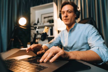 Sunucu kanalı akıllı yayıncı laptopta canlı sosyal medya uygulaması arıyor, kulaklık takıyor ve modern ofis stüdyosundaki mikrofonu kullanıyor. Bireysel.