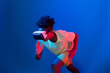 Genç Afrikalı Amerikalı spor koşucusu VR ile egzersiz koşusu koşusu yapıyor mavi neon duvarda yarış koşusu yapıyor metaevren dünyasındaki fütürist teknoloji sanal gerçekliğini birbirine bağlıyor. Entrika.