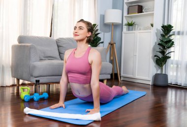 Spor kıyafetleri içinde esnek ve becerikli bir kadın evde egzersiz paspası üzerinde meditasyon pozisyonunda yoga yapıyor. Huzurlu ve huzurlu bir yoga yaşam tarzı..