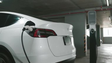 Şehir merkezindeki kapalı otoparkta yavaş çekimde EV elektrikli araba şarj oluyor. Şehir merkezinde sürdürülebilirlik yeşili, yeniden şarj edilebilir elektrikli araç iç organları.
