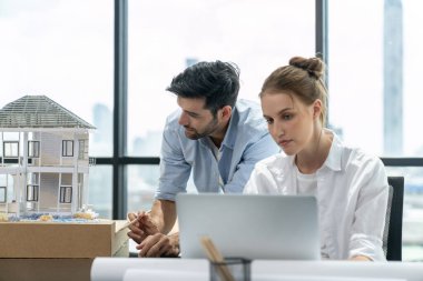 Genç yetenekli proje yöneticisi, modern ofis veya mimarlık stüdyosundaki proje planını kullanarak, Kafkas mühendisi ev modunu incelerken dizüstü bilgisayar kullanarak çalışıyor. İnşaat mühendisliği, yaratıcı tasarım. İzleme.