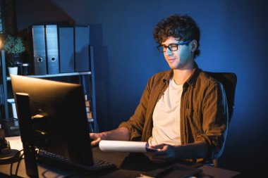 Genç işadamı, Neon Light Modern Ofis 'teki yeni proje surround çalışma masası için kağıt üzerinde tasarım düşünüyor. E-posta ile hediye göndermeden önce not defterine yeni bir iş düşünüyorum. Toplayıcı.