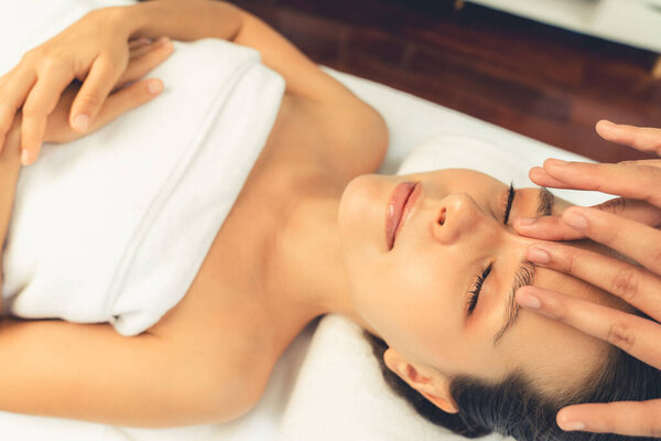 Кавказская женщина наслаждается расслабляющим антистрессовым массажем головы и расслабляющим отдыхом на коже лица в дневном спа-салоне современного света в роскошном курорте или спа-салоне отеля. Quiescent