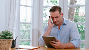 İş adamı, evde dizüstü bilgisayarla iş problemini çözmeye çalışıyor, evde masasında oturmuş, stresli ve hayal kırıklığına uğramış bir ifadeyle probleme çözüm bulmaya çalışıyor. Eşzamanlama