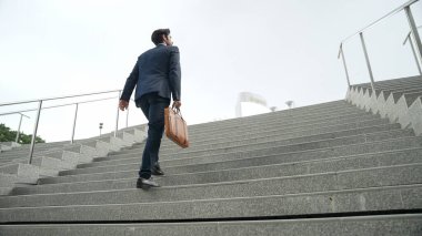 Akıllı bir iş adamının elinde çantayla merdivenlerden yukarı çıkışının en üst görüntüsü. Profesyonel proje yöneticisi merdivenlerden çıkıp işyerine gidiyor. Yeteneklerini arttırmak, terfi almak, seyahat etmek. Sevinçli..