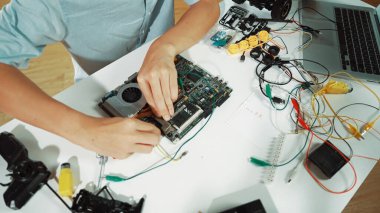 Masadaki elektronik aletle ana kartı tamir eden çocuğa yakın çekim. Elektronik teçhizatla lise öğrencilerinin elektrik panosunun en üst görüntüsü, kablo aletleri masanın etrafına saçılmış. Öğretim.
