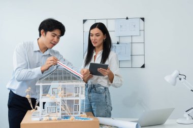 Güzel, genç, beyaz bir proje yöneticisi Asyalı mühendise, mühendislik masasında ev modelini ölçerken tablet kullanarak bina detaylarını anlattı. Tertemiz.