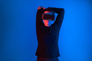 Zeki sporcu VR giyip tüm vücudunu mavi neon ışıklı arka plan üzerinde gererek dijital fütüristik teknoloji sanal gerçekliğini egzersiz konseptine bağlıyor. Entrika.