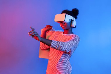 Canlı dijital fütüristik teknoloji meta metasında hologram uygulaması güzellik bezi ürünü üzerinde alışveriş poşeti tutarken İnternet üzerinden alışveriş yapan genç Afrikalıların keyfini çıkarın. Entrika.