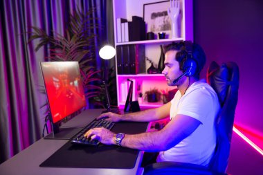 Kulaklık takan akıllı oyun flaması hafta sonu neon dijital siber ışıklandırma odasında son yaşam tarzı yarışmasında şampiyon olmak için bilgisayar ekranında araba yarışı oynamaktan zevk alır. Tahmin et..