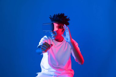 VR kullanan Afro-Amerikan oyun oyuncusu araba yarışı oyunu oynayan meta izole edilmiş mavi neon ışıklı arka duvar fütüristik teknoloji sanal gerçeklik yeni dünyayı birbirine bağlıyor. Entrika.