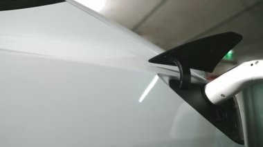 Yavaş çekim yakın EV elektrikli araba şarj istasyonunda fişe takılı, şehir merkezindeki alışveriş merkezinin otoparkında şarj bataryasını şarj ediyor. Elektrikli araç iç organları için temiz yeşil sürdürülebilir enerjisi var.