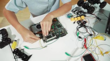 Masadaki elektronik aletle ana kartı tamir eden çocuğa yakın çekim. Elektronik ekipmanlı bir lise öğrencisi elektrik panosunun en üst görüntüsü, kablo aletleri masanın etrafına saçılmış. Öğretim