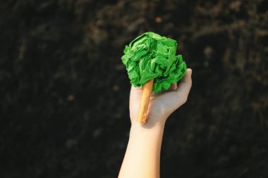 Çocuk, gübrelenmiş toprağı, sürdürülebilir ekoloji ve ormanlaşmalı daha yeşil çevre için büyüyen ve besleyen bitki konseptinin bir parçası olarak kağıt ağacı tutuyor. Döngü