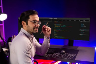 Bilgisayar ekranında yazılım geliştirme kodlu akıllı bilişim geliştiricisi dışarıya bakan bir ekranda poz veriyor, neon ışıklı siber ofiste çevrimiçi web sitesi verilerini sunuyor. Tahmin et..