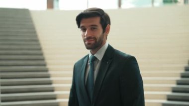 Akıllı iş adamı merdivenlerde kameraya bakıyor. İş elbisesi giyerken kameraya gülümseyen başarılı adamın yakın çekimi. Yönetici, kameraya bak. Hareket eden kamera. Sevinçli..