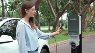 Ulusal Park veya Yaz Ormanı 'ndaki tatil gezisi sırasında EV şarj istasyonundan elektrik aküsü almak için akıllı telefon internet bankacılığı başvurusu yapan bir kadın. Yükselt