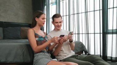 Genç çift, kredi kartıyla ödemek için internet üzerinden ödeme uygulaması ve dijital cüzdan kullanarak yatak odasında oturuyor. Mobil internet üzerinden alışveriş ve modern alımlar. Düzenle