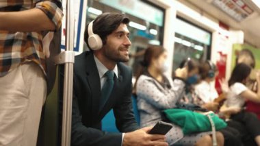 Gülümseyen yakışıklı yatırımcı trende otururken rahatlatıcı müzik dinliyor. Profesyonel iş adamı iş yerine toplu taşıma araçlarıyla giderken müzik dinlemeyi sever. Arka plan bulanık. Sevinçli..