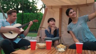 Baba gitar çalarken anne ve kızı bahçede kamp yapıyor. Ebeveynler, genç nesil çapraz kuşak farklılıklarıyla zaman geçirmek için açık hava kamp aktivitelerini kullanıyorlar. Uyumsuzluk.