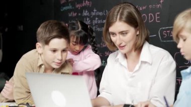 Kafkasyalı öğretmen dizüstü bilgisayar kullanarak mühendislik sistemini açıklarken çeşitli öğrenciler BTMM sınıfında yazılı komut veya kodla karatahtanın önünde elektronik ekipman taşıyorlar. Etkinlik.