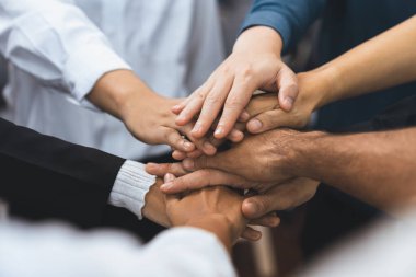 Çeşitli ofis çalışanlarından oluşan bir grup, ofis odasında el ele vererek iş sinerjisini ve iş yerindeki güçlü verimli takım çalışmasını sembolize ediyor. İş çalışanları arasındaki işbirliği ve birlik. Tedbirli