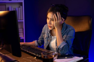 Stresli, genç, güzel Asyalı yaratıcı proje yaratıcısı sosyal medyayı araştırmak için bilgisayara bakıyor ve geceleri daha çok neon modern ofisin planlama kanalı stratejisine ulaşılıyor. Taktik.