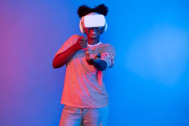 VR kullanan Afrikalı bir oyuncuyu avlamak, meta-evrende silah ateşleme oyunu oynamak, mavi neon ışığını izole etmek, zafer hayvanı avlamak, fütüristik teknoloji hologramı sanal gerçekliği. Entrika.