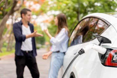 Sonbahar gezisi sırasında sonbahar ormanı EV arabasında elektrikli araba için şarj olan sevimli genç çift. Sonbahar tatilinde çevre dostu seyahat. Yükselt