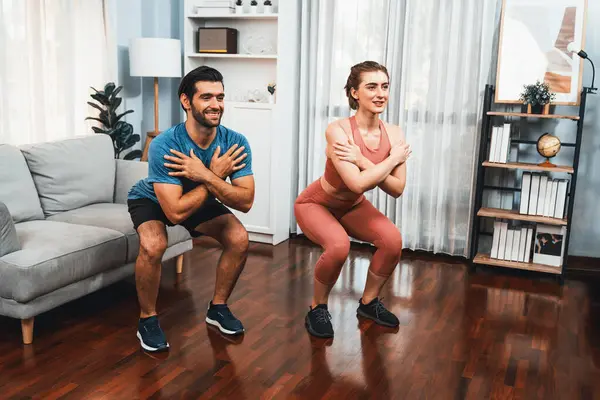 Stock image Athletic and sporty couple doing squat together during home body workout exercise session for fit physique and healthy sport lifestyle at home. Gaiety home exercise workout training concept.