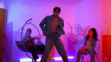 Çok kültürlü bir arkadaş kürsüde otururken Asyalı yetenekli bir dansçı modern müziğe geçiyor. Profesyonel dansçı, hipster takımı tezahürat yaparken ve desteklerken enerjik adımlar atıyor. Mutluluk.