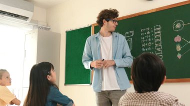 Matematik formülü veya teorisi ile karatahtanın önünde dururken sınıfın etrafına bakan profesyonel akıl hocası. Çeşitli ilköğretim öğrencileri matematik dersinde öğreniyor, çalışıyor ve oturuyor. Pedagoji.