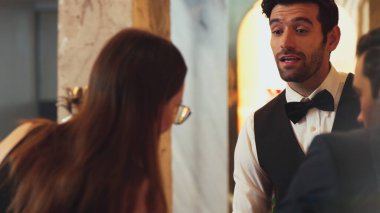 Güzel görünümlü barmen, içki tezgahındaki çiftle samimi bir gülümseme sohbeti yaparken aynı zamanda hoş geldin içkisi ve özel menü listesi öneren çekici profesyonellik. Vinosity.