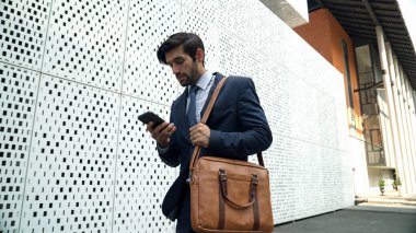 Akıllı yönetici cep telefonuna bakıyor ve takım elbise giyerken sokakta yürüyor. Yetenekli yatırımcı cep telefonuyla satışları kontrol ediyor ya da elinde kahve fincanı tutarken çalışıyor. Beyaz arka plan. Sevinçli..