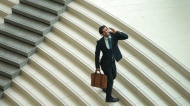 Kameraya bakarken kulaklıktan müzik dinleyen bir iş adamı görüntüsü. Yetenekli proje yöneticisi kameraya gülümserken merdivenlerden iniyor. Beyaz arka plan. Modern dans. Sevinçli..