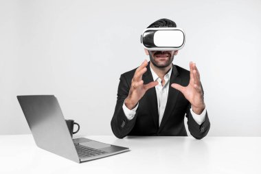 Profesyonel proje yöneticisi dizüstü bilgisayar başında otururken VR gözlüğü kullanıyor. Görsel gerçeklik kulaklığı takan yetenekli bir iş adamı metaevren ya da görsel dünyayı birbirine bağlıyor. Yenilik. Sapma.